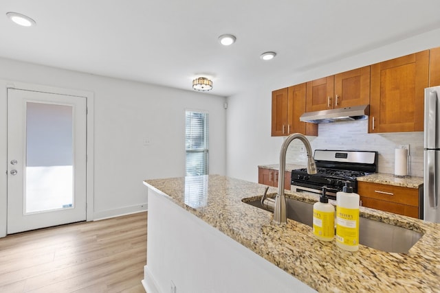 5820 Berkman Dr Unit 116, Austin, TX 78723 - kitchen with under cabinet range hood, appliances with stainless steel finishes, brown cabinets, light wood finished floors, and decorative backsplash