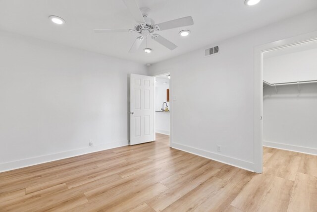 unfurnished bedroom with light wood-type flooring, a walk in closet, a closet, and ceiling fan