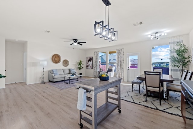 living room with ceiling fan with notable chandelier and light hardwood / wood-style flooring