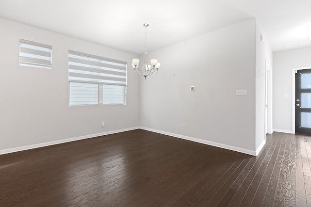 spare room featuring an inviting chandelier and dark hardwood / wood-style flooring