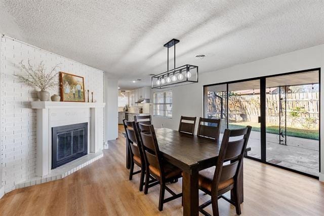 dining space with a fireplace, light wood-type flooring, and a textured ceiling