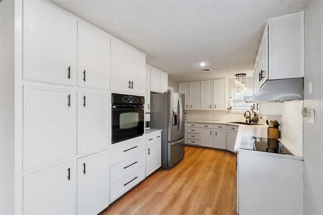 kitchen featuring black appliances, sink, a textured ceiling, light hardwood / wood-style floors, and white cabinetry