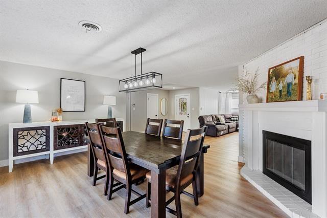 dining space with light hardwood / wood-style floors, a textured ceiling, and a brick fireplace