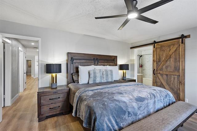 bedroom featuring a textured ceiling, a barn door, ceiling fan, and wood-type flooring