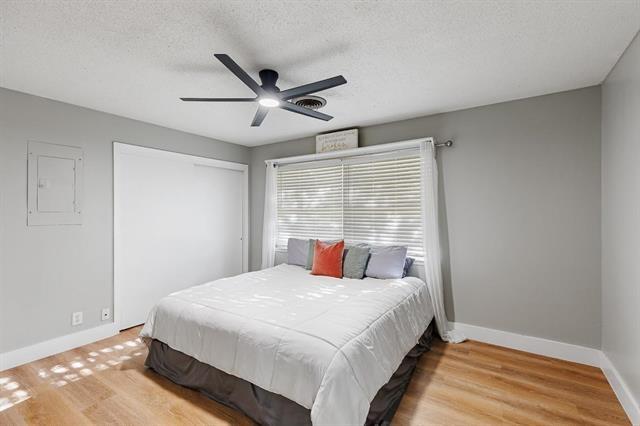 bedroom featuring ceiling fan, wood-type flooring, a textured ceiling, and electric panel