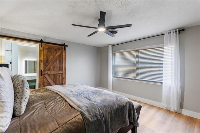 bedroom with ceiling fan, a barn door, a textured ceiling, and light hardwood / wood-style flooring