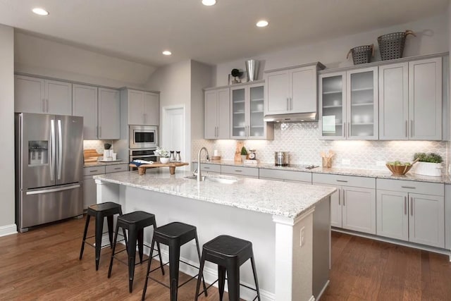 kitchen featuring a center island with sink, light stone counters, sink, and stainless steel appliances