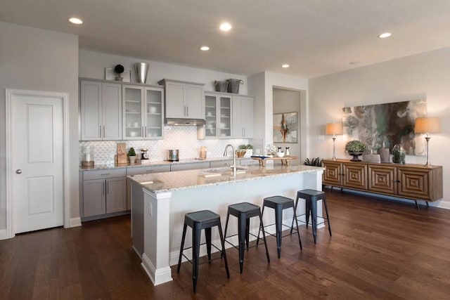 kitchen featuring sink, light stone counters, dark hardwood / wood-style floors, a kitchen island with sink, and a breakfast bar