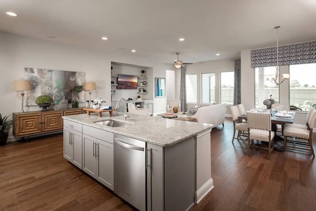 kitchen with sink, light stone counters, stainless steel dishwasher, decorative light fixtures, and a center island with sink