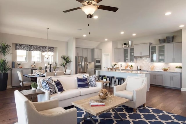 living room featuring ceiling fan with notable chandelier, dark wood-type flooring, and sink