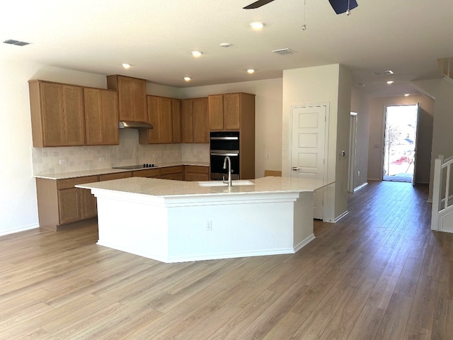 kitchen with visible vents, backsplash, a sink, a large island with sink, and black appliances