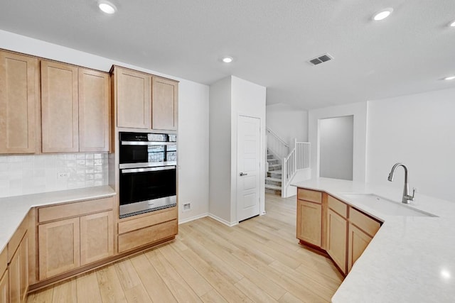 8004 Tranquil Glade Trl, Austin, TX 78744 - kitchen with double oven, a sink, light wood-type flooring, tasteful backsplash, and light brown cabinets