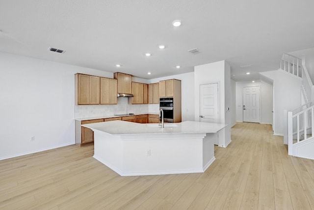 8004 Tranquil Glade Trl, Austin, TX 78744 - kitchen featuring multiple ovens, an island with sink, light countertops, light wood-style floors, and black electric stovetop