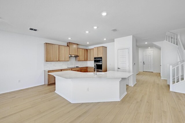 8004 Tranquil Glade Trl, Austin, TX 78744 - kitchen featuring stainless steel double oven, a kitchen island with sink, light countertops, light wood-style floors, and backsplash