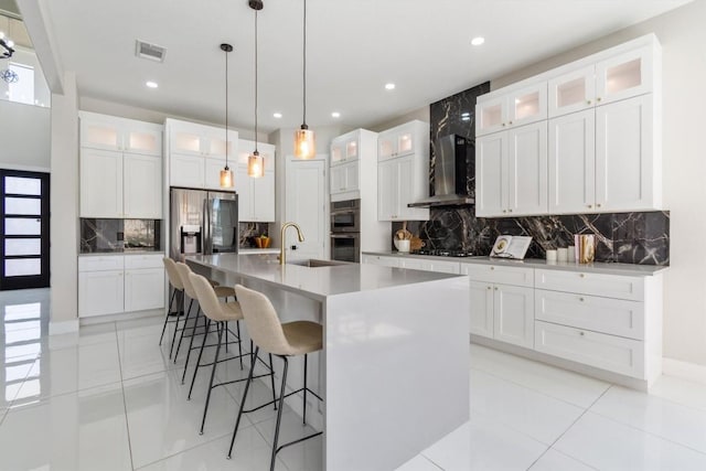kitchen featuring decorative backsplash, a breakfast bar, wall chimney exhaust hood, a sink, and stainless steel appliances