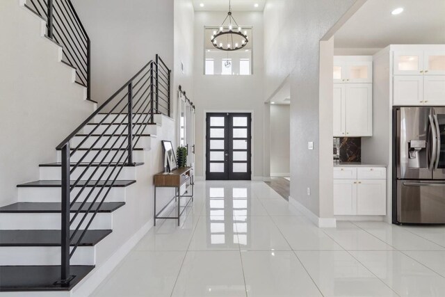 foyer entrance featuring a high ceiling, light tile patterned floors, a chandelier, and french doors