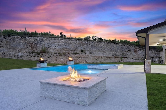 pool at dusk with ceiling fan, a patio area, a fire pit, and an in ground hot tub