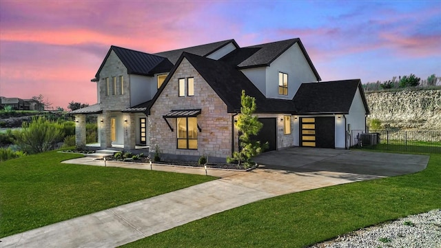 modern farmhouse style home featuring a standing seam roof, driveway, a lawn, fence, and stone siding