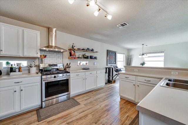 kitchen featuring backsplash, wall chimney exhaust hood, pendant lighting, white cabinets, and stainless steel range with gas cooktop