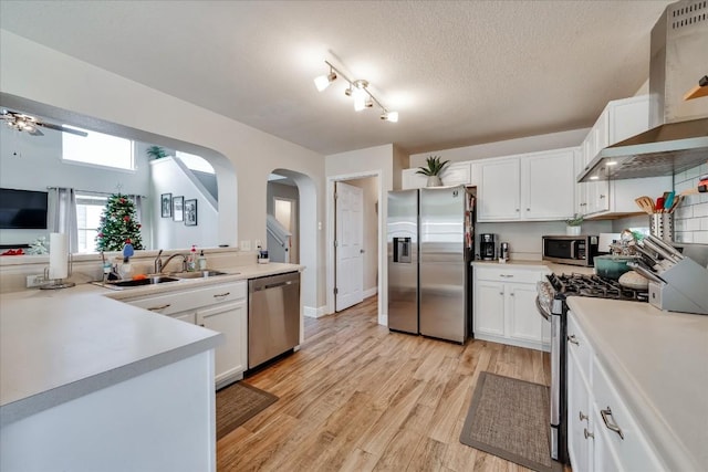 kitchen featuring appliances with stainless steel finishes, sink, wall chimney range hood, white cabinets, and light hardwood / wood-style floors