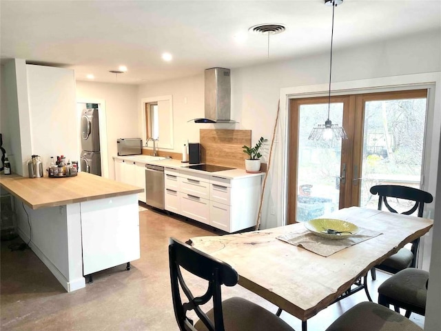 kitchen with stacked washer and dryer, hanging light fixtures, stainless steel dishwasher, wall chimney exhaust hood, and white cabinetry