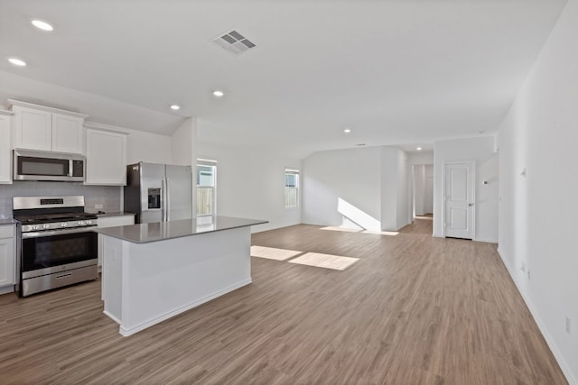 kitchen with a center island, backsplash, white cabinets, light hardwood / wood-style flooring, and stainless steel appliances