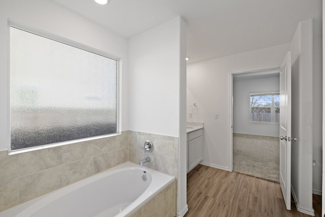 bathroom featuring vanity, wood-type flooring, and a relaxing tiled tub