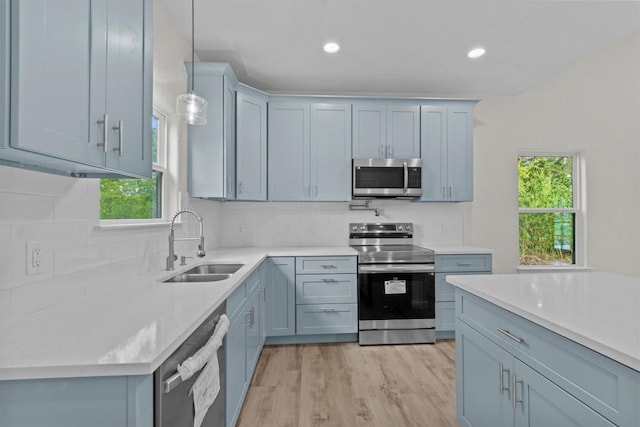 kitchen featuring backsplash, stainless steel appliances, sink, decorative light fixtures, and light hardwood / wood-style floors