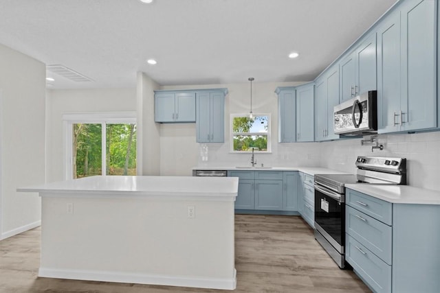 kitchen featuring appliances with stainless steel finishes, light wood-type flooring, sink, pendant lighting, and a center island