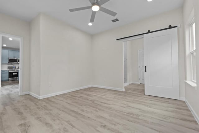 unfurnished room with ceiling fan, a barn door, and light hardwood / wood-style flooring