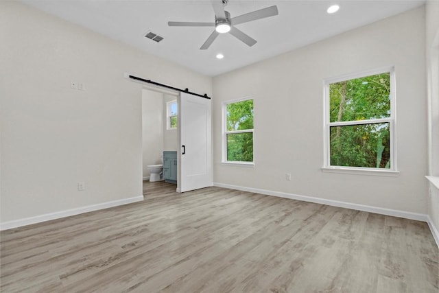 unfurnished bedroom with a barn door, ensuite bathroom, light hardwood / wood-style flooring, and ceiling fan