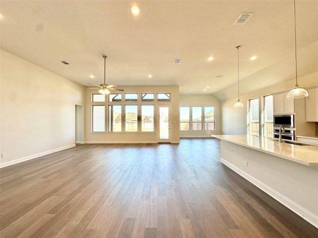 unfurnished living room featuring ceiling fan, vaulted ceiling, dark wood-type flooring, and sink