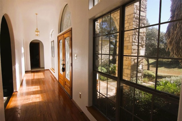 hall with arched walkways, a towering ceiling, and hardwood / wood-style flooring