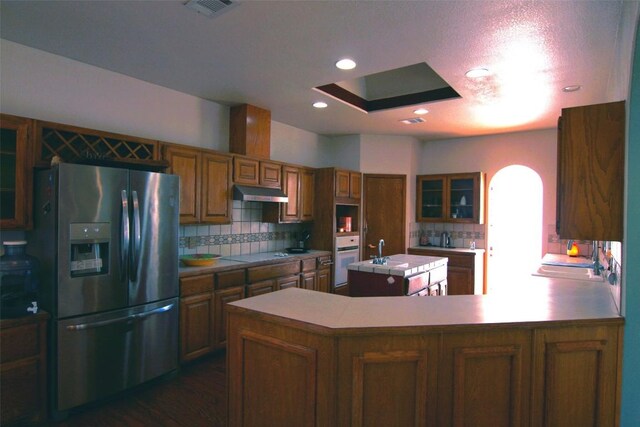 kitchen featuring a center island, white oven, cooktop, stainless steel fridge with ice dispenser, and decorative backsplash