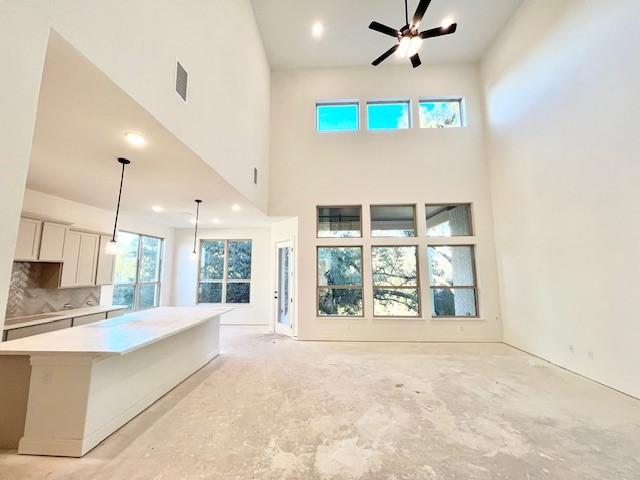 unfurnished living room with ceiling fan and a towering ceiling