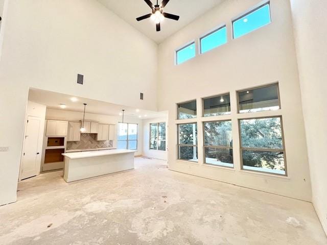 unfurnished living room featuring ceiling fan and a high ceiling