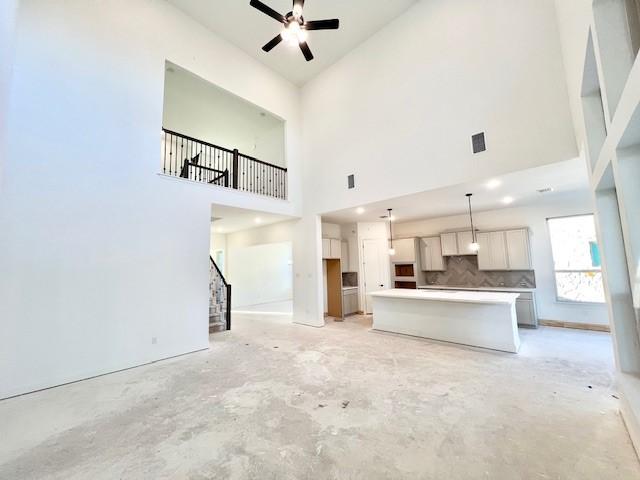 unfurnished living room with ceiling fan and high vaulted ceiling