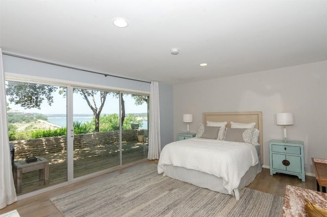 bedroom with a water view, wood-type flooring, and access to outside