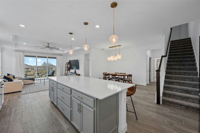 kitchen with a breakfast bar, gray cabinetry, a tray ceiling, a kitchen island, and pendant lighting