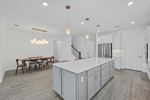 kitchen featuring hanging light fixtures, a center island, stainless steel refrigerator, and light hardwood / wood-style flooring