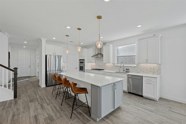 kitchen featuring pendant lighting, white cabinetry, a center island, stainless steel appliances, and wall chimney range hood