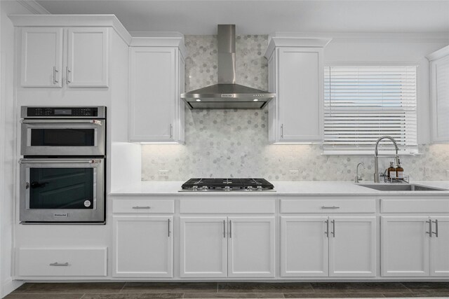 kitchen featuring appliances with stainless steel finishes, sink, white cabinets, and wall chimney exhaust hood