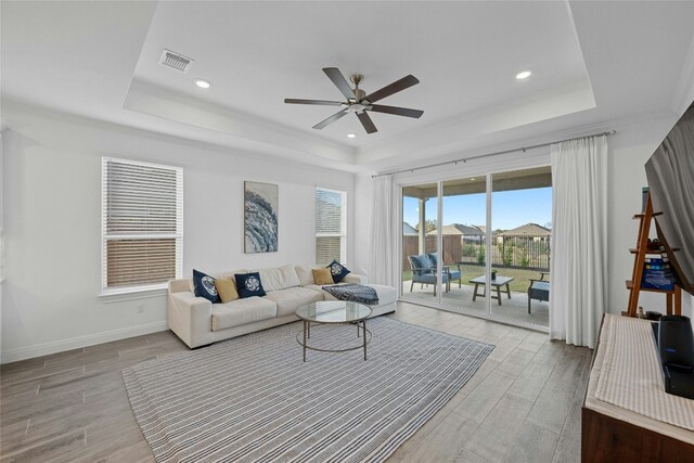 living room with a tray ceiling, light hardwood / wood-style floors, and ceiling fan