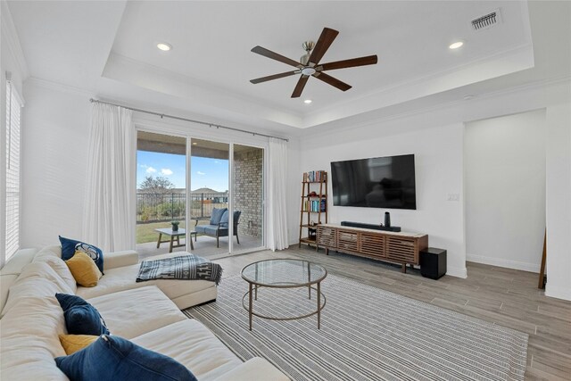 living room featuring hardwood / wood-style floors, a tray ceiling, ornamental molding, and ceiling fan