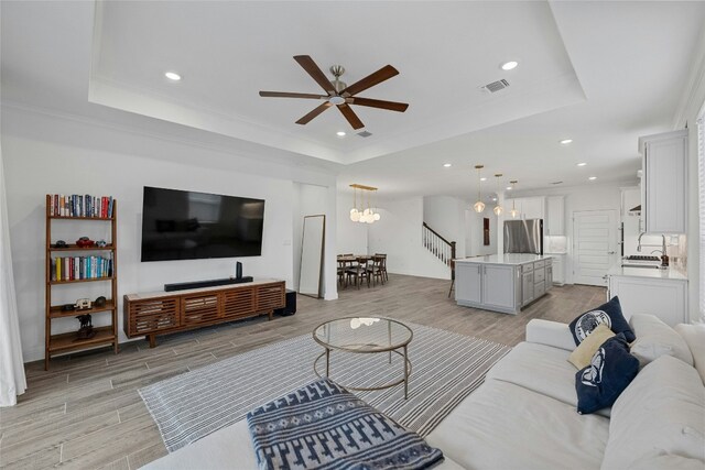 living room with a tray ceiling, light hardwood / wood-style flooring, and ceiling fan with notable chandelier