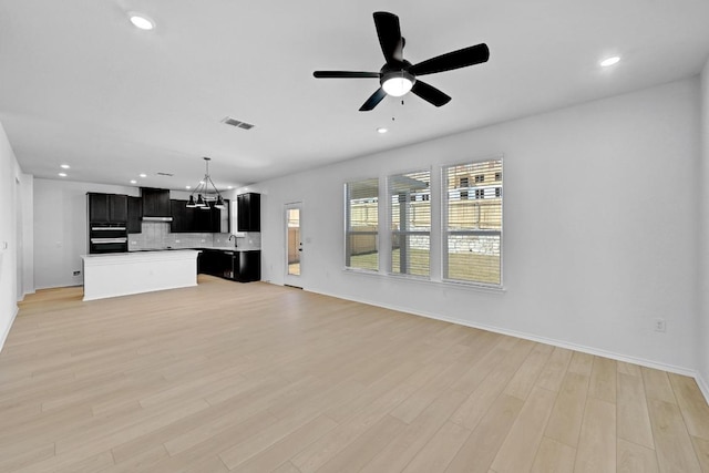 unfurnished living room with light wood finished floors, visible vents, ceiling fan with notable chandelier, recessed lighting, and a sink