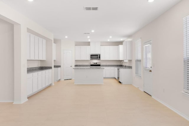 kitchen featuring visible vents, a center island, white cabinets, stainless steel appliances, and a sink