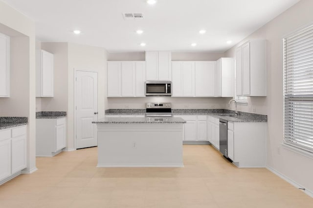 kitchen with light stone counters, recessed lighting, a sink, appliances with stainless steel finishes, and a center island