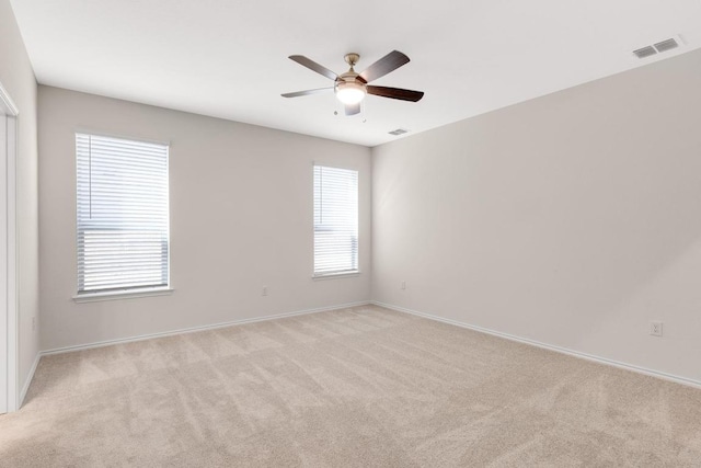 empty room with visible vents, light colored carpet, baseboards, and ceiling fan