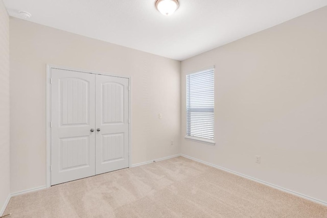 unfurnished bedroom featuring a closet, light colored carpet, and baseboards